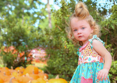 Portrait of girl standing by pumpkins at park during autumn