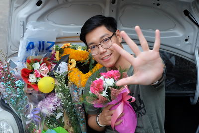 Portrait smiling of young man gesturing with bouquets in car trunk