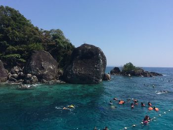 People swimming in sea against clear blue sky