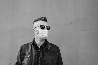 Man wearing sunglasses and mask while standing against wall