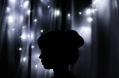 Close-up of silhouette woman against illuminated string lights in darkroom