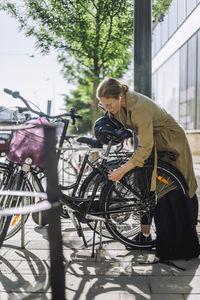 Businesswoman unlocking bicycle while standing at parking station