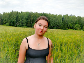 Portrait of beautiful young woman standing on field against sky