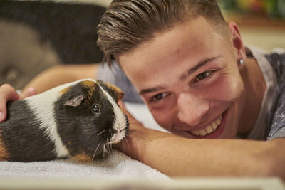 Close-up of smiling man playing with guinea pig on bed at home