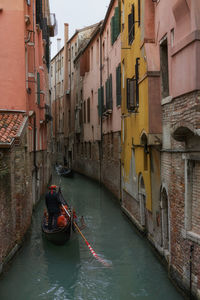 Rear view of man sailing boat in canal amidst buildings