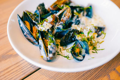 Close up of freshly cooked mussles in a plate with ingredients.