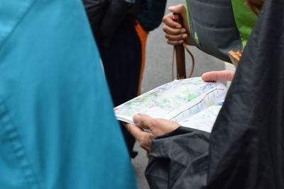 Midsection of people analyzing map while standing outdoors