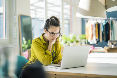 Fashion designer sitting at desk in her studio looking at laptop