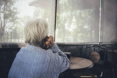 Rear view of old woman sitting by window at home. concept loneliness, dementia, abuse, sadness.