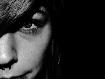 Portrait of young woman with piercing against black background