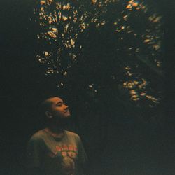 Portrait of young man looking away against trees