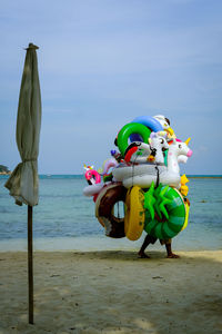 An obscured man walking with mountain of inflatable toys with sea in background 