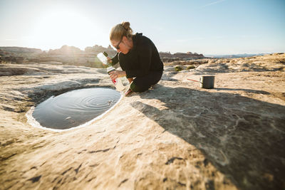 Female camper collects water for cooking from a shallow puddle