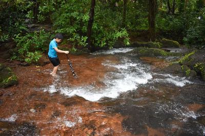 Boy standing in stream at forest