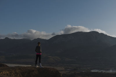 Back view of woman standing on a mountain with view of clouds and mountains on background