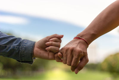 Close-up of couple holding hands against sky