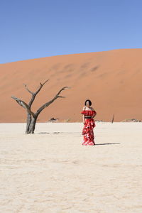 Woman standing on sand against clear blue sky