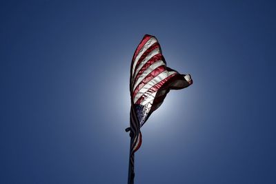 An american flag blows in the wind while backlit by the sun.