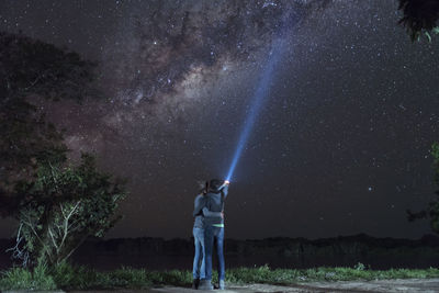 Rear view of couple with arm around lightning torch against sky at night