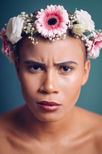 Close-up portrait of young woman wearing flowers against blue background