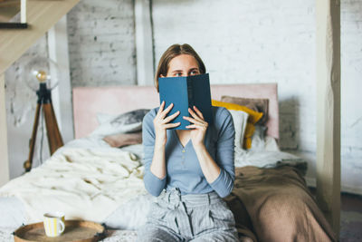 Full length of woman using mobile phone while sitting on bed