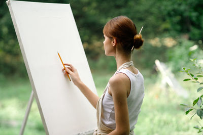 Rear view of woman using digital tablet while sitting on field