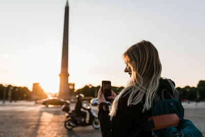 Woman taking a picture with her mobile phone at place de la concorde in paris during sunset