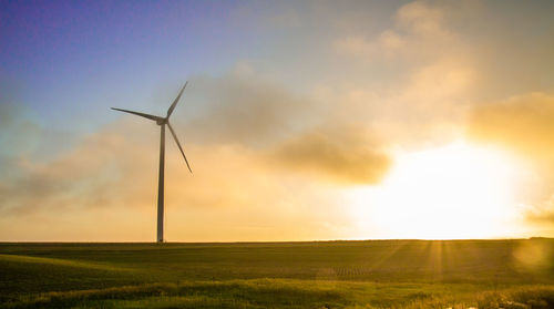Low angle view of windmill on grassy field at sunset