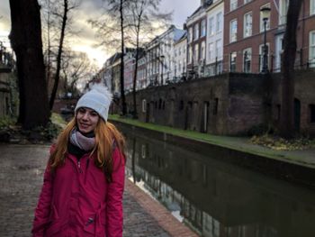 Portrait of young woman standing by canal in city