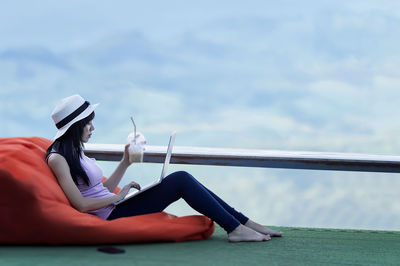 Woman sitting on swing against sky