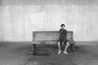 Full length portrait of woman sitting on bench against wall