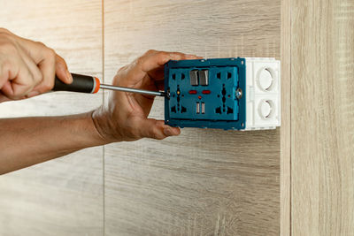 Electrician is using a screwdriver to install the electric power socket in to a plastic outlet box