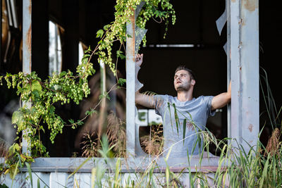 Young man looking away while standing against plants