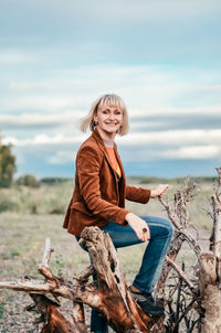 Full length of smiling young woman sitting on land against sky