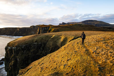 Rear view of man standing on rock against sky