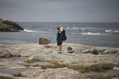 Man standing on rock at sea shore against sky