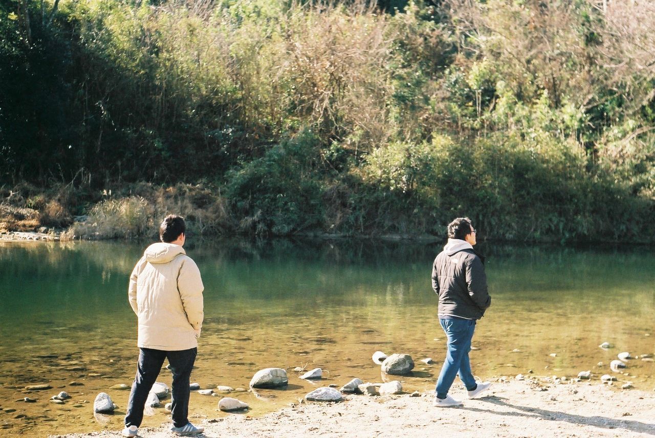 REAR VIEW OF MAN STANDING WITH DOG IN LAKE