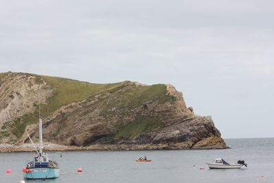 Boats moored on sea by mountains against sky