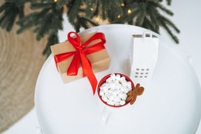 Christmas still life of present gift box, cocoa with marshmallow on white table, top view