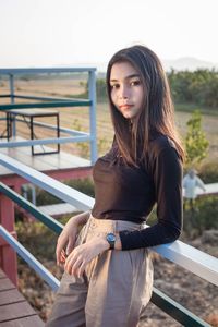 Portrait of young woman standing against railing