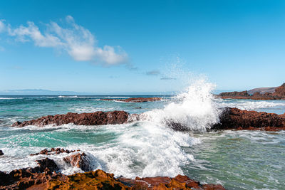 Waves splashing on rocks at shore against sky