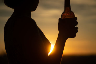 Silhouette woman holding bottle against sky during sunset