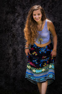 Portrait of smiling young woman standing against wall