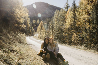 Smiling friends sitting on footpath in forest