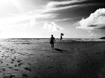 Silhouette man with surfboard walking at beach against cloudy sky