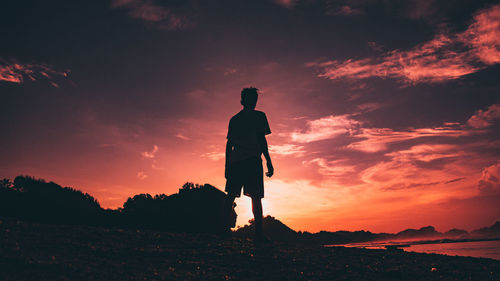 Silhouette man standing on field against sky during sunset