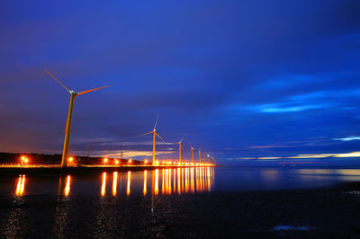 Illuminated commercial dock by sea against blue sky