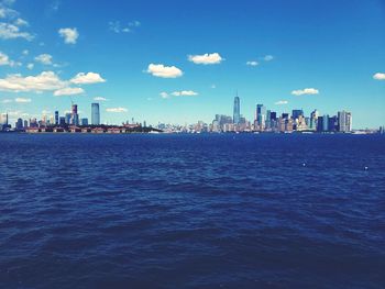 Sea by buildings in city against blue sky