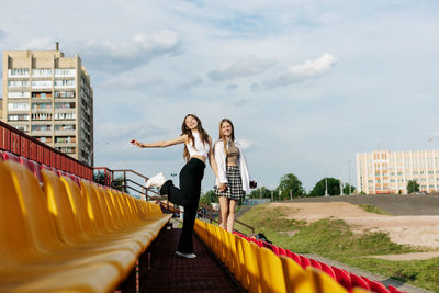 Two teenage girls walk together through the stands of the school stadium, talking, holding hands