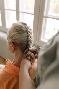 Midsection of young female caregiver braiding senior woman's hair at nursing home